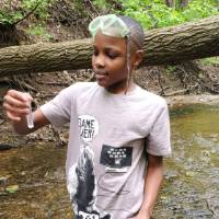 Student stands in stream and looks at sample of water